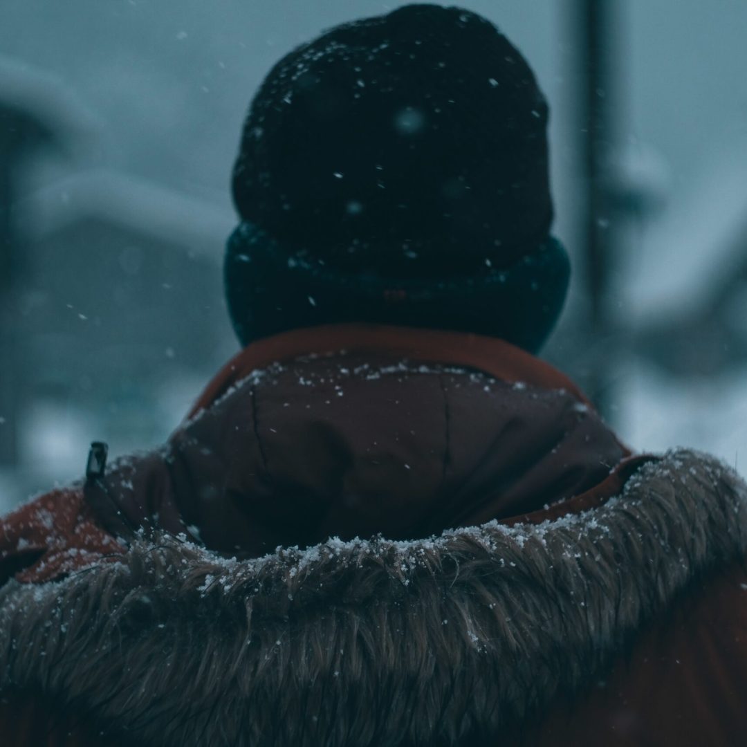The back of a man with a hooded coat and a beanie during winter