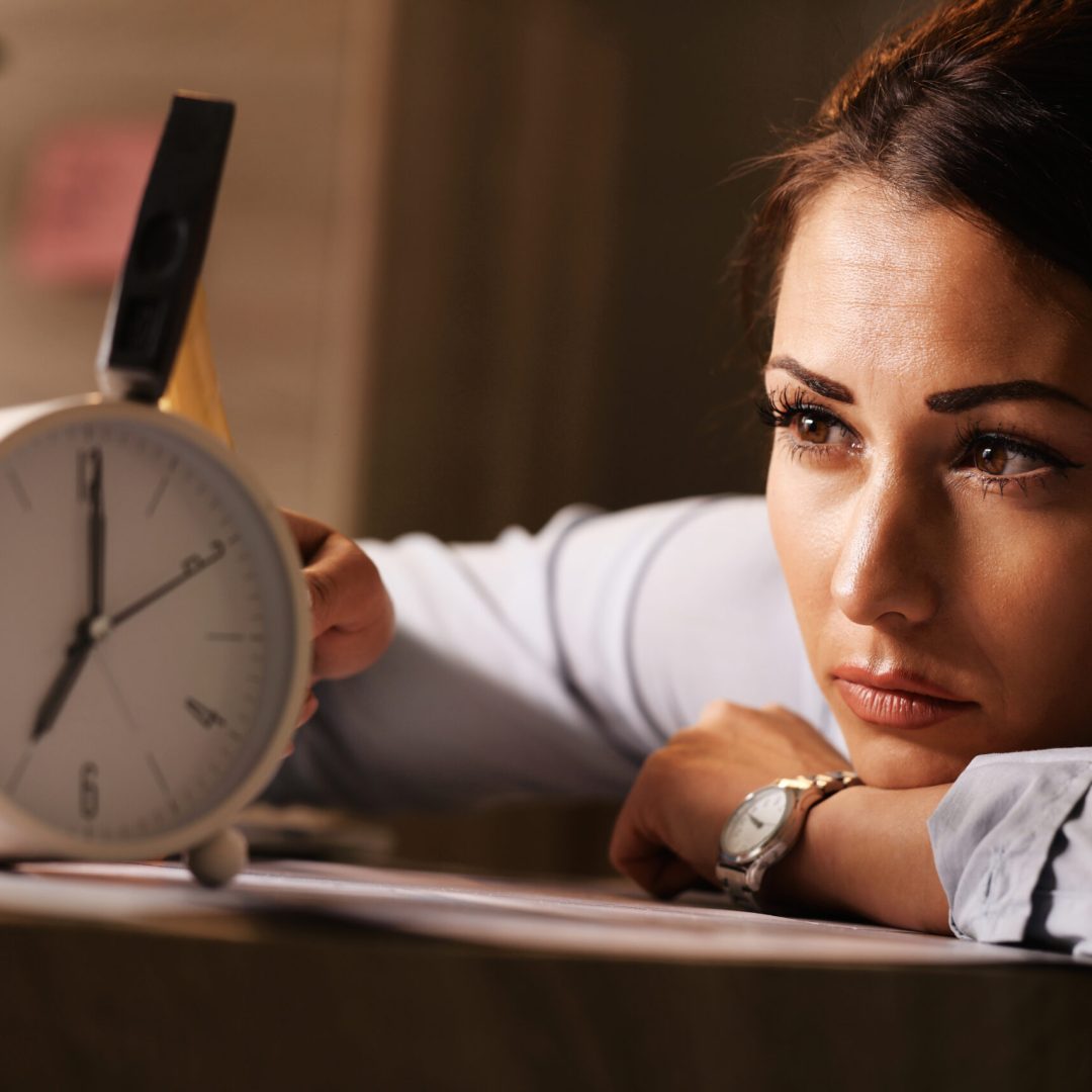 Displeased businesswoman hitting alarm clock with hammer in the office.