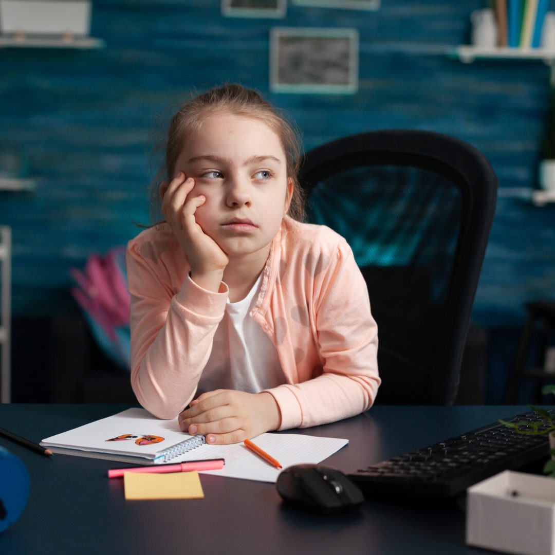 Little girl doing homework feeling bored and sad at home desk. Smart child with overload problem being exhausted from class notes. Overwhelmed from studying and school lesson work